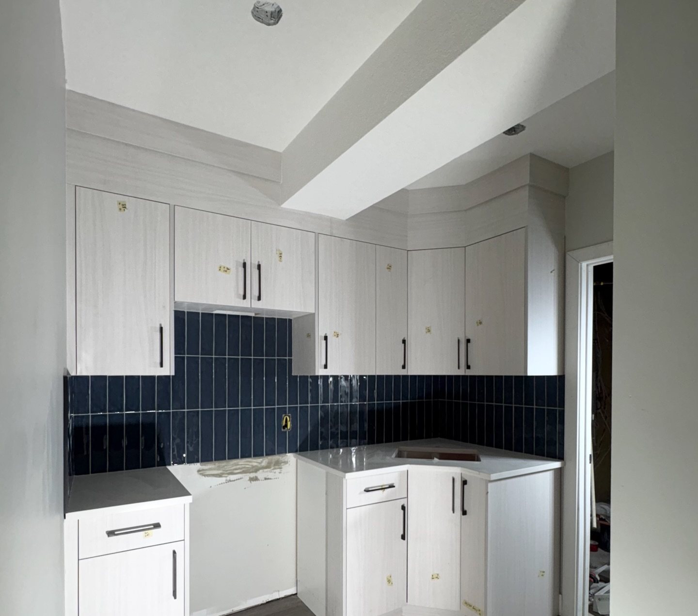 Basement kitchen with white cabinets and installed navy tile backsplash